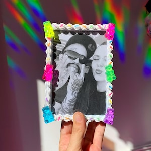 Peut inclure: Un cadre photo blanc avec une photo en noir et blanc d'un couple. Le cadre est décoré d'oursons en gélatine colorés.