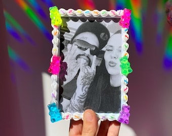 May include: A white picture frame with a black and white photo of a couple. The frame is decorated with colorful gummy bears.