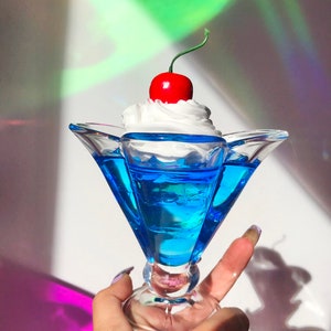 K&ouml;nnte beinhalten: Eine blaue Glasschale in Form einer Eiswaffel mit einer wei&szlig;en Schlagsahne-F&uuml;llung und einer roten Kirsche.