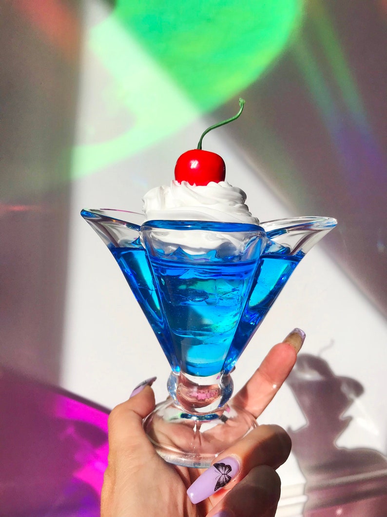 K&ouml;nnte beinhalten: Eine blaue Glasschale in Form einer Eiswaffel mit einer wei&szlig;en Schlagsahne-F&uuml;llung und einer roten Kirsche.