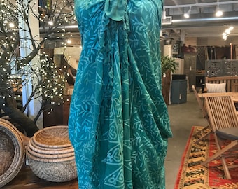 May include: A teal blue sarong with a white floral pattern. The sarong is tied around a mannequin and has a fringe trim.