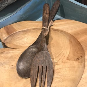 Puede incluir: Un juego de utensilios de servicio de madera marrón oscuro, una cuchara y un tenedor, en una bandeja de servicio de madera marrón claro.