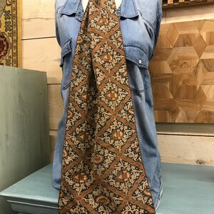 May include: A brown and cream patterned silk scarf with tassels. The scarf has a geometric design with floral motifs.
