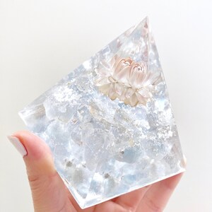 May include: A clear crystal pyramid with a pressed dried flower inside. The flower is a pale pink colour and has a delicate texture.