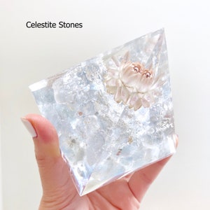 May include: A clear, iridescent pyramid-shaped crystal with a dried white flower inside. The crystal is labelled "Celestite Stones".