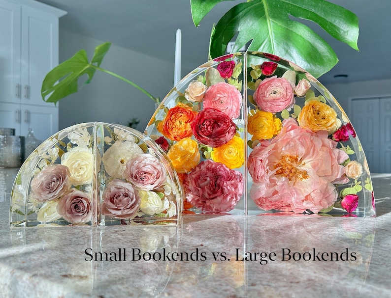 May include: Clear resin bookends, small and large, each featuring a half-circle design. The bookends are filled with colorful flowers in shades of pink, yellow, and red. The text "Small Bookends vs. Large Bookends" is at the bottom.