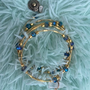 Op de afbeelding: Goudkleurige, met draad omwikkelde armbanden met blauwe kristallen kralen en een heldere kwartshanger met een sterrenbedel. Er is ook een zilveren ring met de woorden "MADE WITH LOVE".