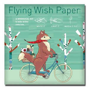 May include: A whimsical kit titled "Flying Wish Paper" features a brown fox riding a blue bicycle, carrying gifts in a basket. The fox wears a red scarf. The background is light green with white trees. Text reads "Write it, Light it, Watch it Fly."
