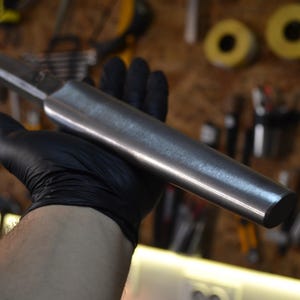 May include: A close-up of a long, silver, cylindrical metal rod with a rounded end. The rod is being held by a gloved hand.