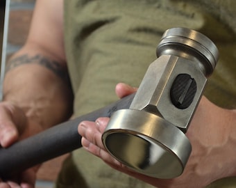 May include: A steel hammer with a dark handle. The hammer head has a flat striking face and a rounded face. The hammer is held by a person wearing a green apron.