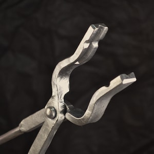 Puede incluir: Primer plano de un par de tenazas plateadas con un mango curvo. Las tenazas son de metal y tienen un acabado liso.