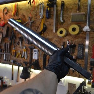 Könnte beinhalten: Ein langer, silberner Metallstab mit einem quadratischen Ende. Der Stab ist konisch, wird zum quadratischen Ende hin dünner. Der Stab wird in einer behandschuhten Hand gehalten.