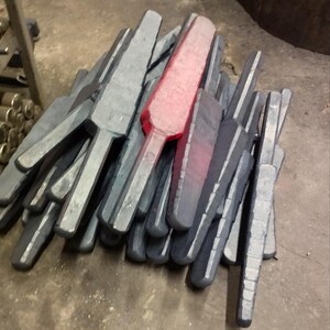 May include: A pile of metal parts, some are a dark gray color and some are a bright red color. The parts are shaped like a long, thin rectangle with a cross at one end.