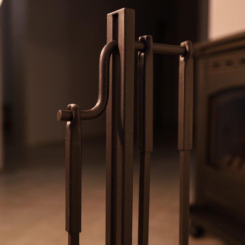 May include: A set of four black metal fireplace tools with a stand. The tools include a poker, tongs, shovel, and brush. The stand has a hook for hanging the tools.