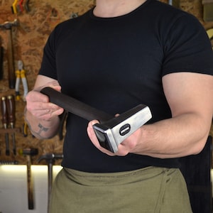 May include: A heavy-duty, steel-headed hammer with a dark wooden handle. The hammer's head is rectangular with a flat striking surface and a rounded edge. The handle is thick and appears to be made of a dark-stained wood. The hammer is designed for heavy-duty tasks.