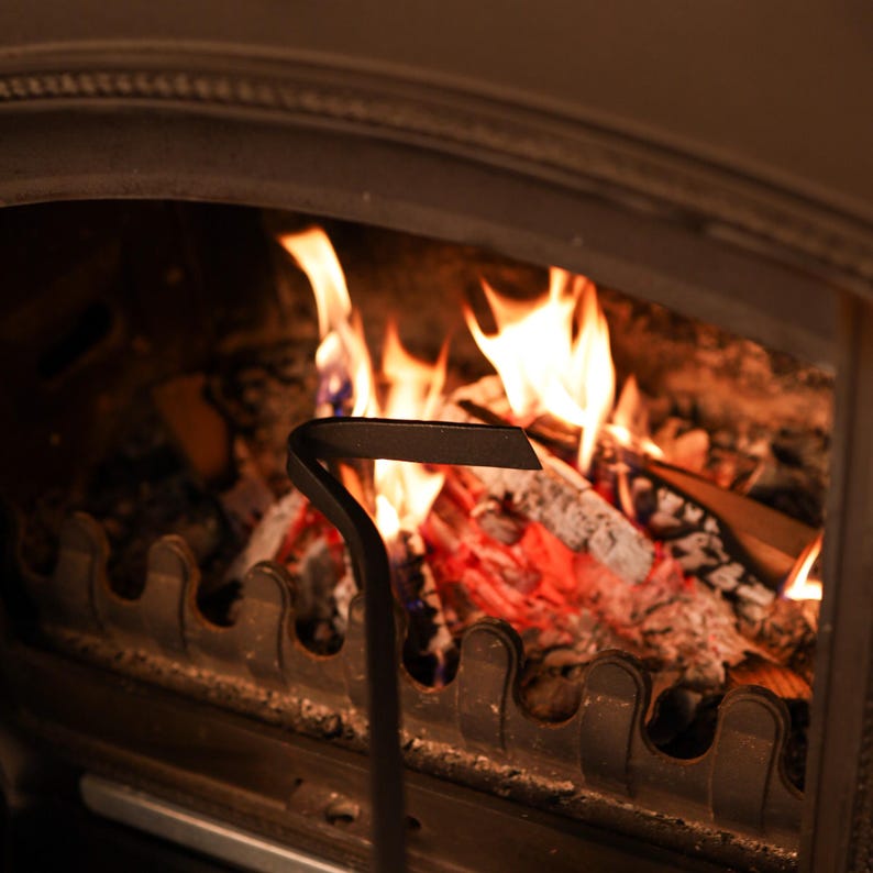 May include: A close-up of a fireplace with a fire poker in the foreground. The fire is burning brightly and the poker is made of metal.