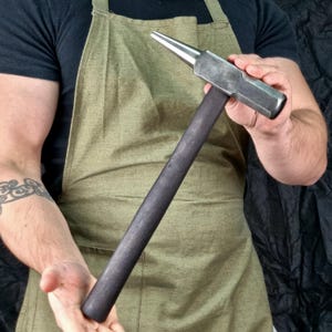 Peut inclure: Un marteau à long manche avec une tête arrondie et un manche en bois. Le marteau est en métal et a une finition argentée.