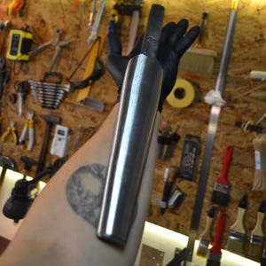 May include: A long, silver metal rod with a rounded end. The rod is being held by a gloved hand.