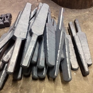 May include: A pile of gray metal wedges, likely used for splitting wood or other materials. The wedges are stacked in a random order, with some of them pointing upwards and others pointing downwards.