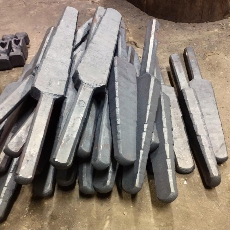May include: A pile of gray metal wedges, likely used for splitting wood or other materials. The wedges are stacked in a random order, with some of them pointing upwards and others pointing downwards.