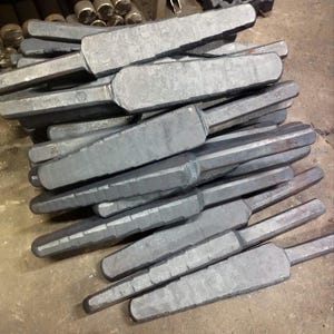 May include: A pile of gray metal rods with a slightly pointed end. The rods are stacked on top of each other and are all the same size.