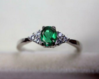May include: A silver ring featuring a large oval green gemstone surrounded by smaller white gemstones.