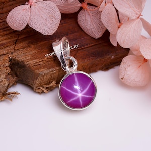 Könnte beinhalten: Ein silberner Anhänger mit einem runden, rosafarbenen Stern-Saphir-Edelstein mit einem sechszackigen Stern in der Mitte.