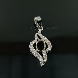 Puede incluir: Pendiente de plata con un engaste ovalado rodeado de peque&ntilde;as piedras transparentes. El pendiente tiene la forma de una llama estilizada.