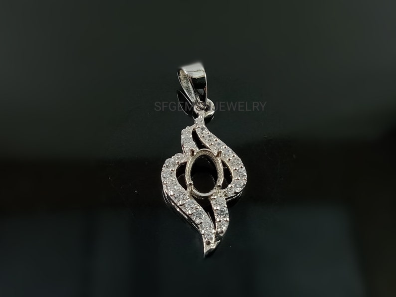 Puede incluir: Pendiente de plata con un engaste ovalado rodeado de peque&ntilde;as piedras transparentes. El pendiente tiene la forma de una llama estilizada.