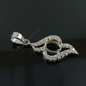 Puede incluir: Pendiente de plata con una montura redonda engastada con peque&ntilde;as piedras transparentes. El pendiente tiene forma de llama y tiene una anilla en la parte superior.