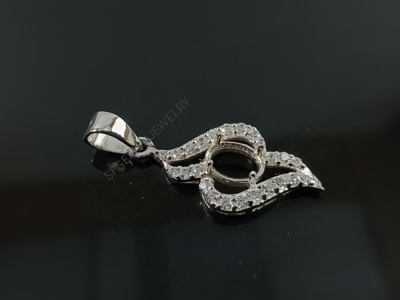 Puede incluir: Pendiente de plata con una montura redonda engastada con peque&ntilde;as piedras transparentes. El pendiente tiene forma de llama y tiene una anilla en la parte superior.