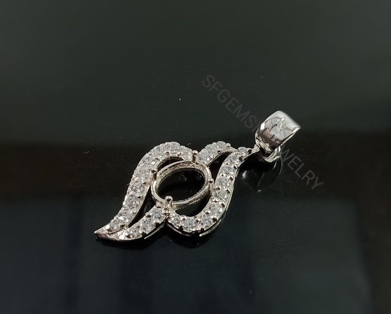 Puede incluir: Pendiente de plata con un engaste de piedra transparente rodeado de peque&ntilde;as piedras transparentes. El pendiente tiene forma de ola estilizada y tiene una anilla en la parte superior. El pendiente est&aacute; marcado con "SFGEMS JEWELRY".