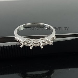 Op de afbeelding: Een zilveren ringbezetting met drie griffen voor ovale edelstenen. De ringband is versierd met kleine ronde stenen.