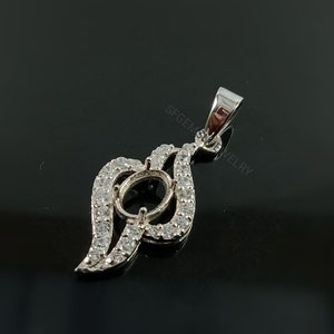 Puede incluir: Pendiente de plata con un engaste ovalado transparente rodeado de peque&ntilde;as piedras transparentes. El pendiente tiene la forma de una hoja estilizada con una anilla en la parte superior.