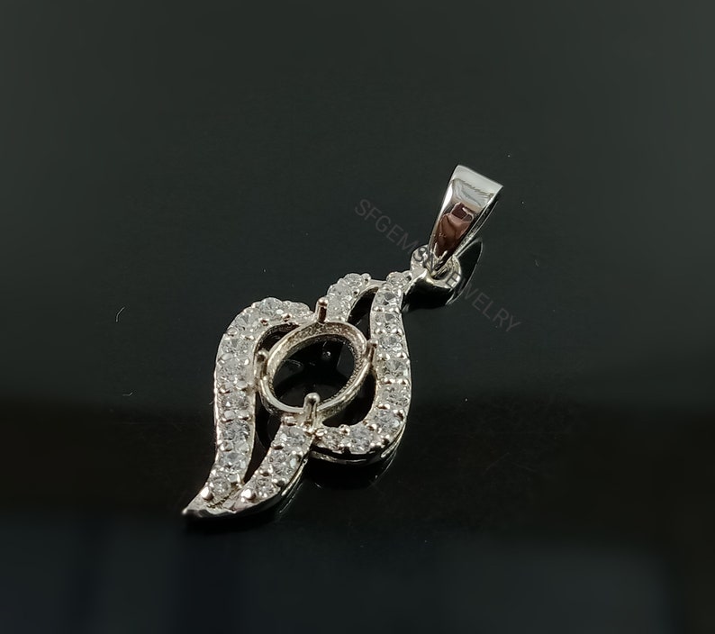 Puede incluir: Pendiente de plata con un engaste ovalado transparente rodeado de peque&ntilde;as piedras transparentes. El pendiente tiene la forma de una hoja estilizada con una anilla en la parte superior.