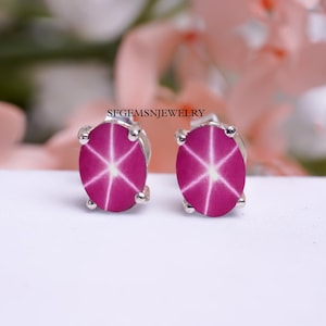 May include: A pair of silver stud earrings with pink star sapphires. The sapphires have a star-like pattern in the center.