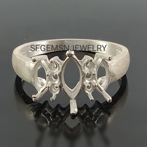 May include: Silver ring setting with a marquise shaped center stone and four prongs on each side. The ring band is smooth and has the text "SFGEMSNJEWELRY" engraved on the inside.