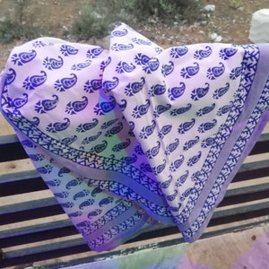 May include: A white fabric with a blue paisley pattern and a blue border. The fabric is draped over a black metal railing. The paisley design is repeated across the fabric's surface.
