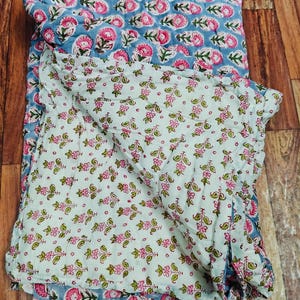 Può includere: Un trapunta di cotone blu e bianco con stampa floreale. La trapunta è piegata a metà e il motivo floreale è visibile su entrambi i lati.