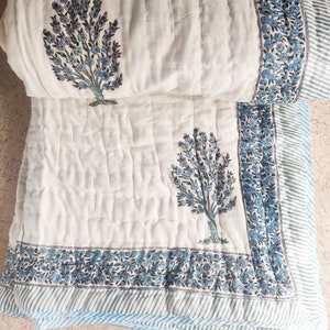 May include: White cotton quilt with a blue floral print. The quilt has a border of blue and white stripes.