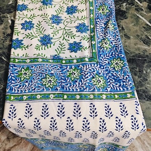 May include: A white cotton tablecloth with a blue and green floral print. The tablecloth has a border with a repeating pattern of leaves and flowers.