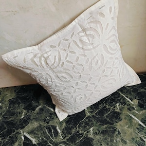 May include: White cotton pillow cover with a delicate floral pattern cut out of the fabric. The pillow cover is on a green marble surface.