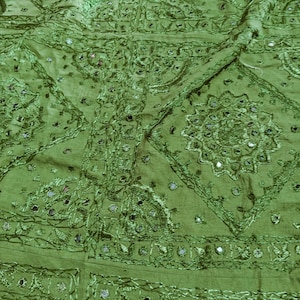 Puede incluir: Tela verde con bordados intrincados y adornos de espejo. La tela tiene un patrón geométrico con un diseño floral. La tela es un textil indio tradicional.
