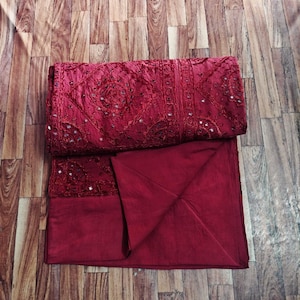 Peut inclure: Un ensemble de tissu bordeaux plié, possiblement des vêtements, avec des broderies complexes et de petits ornements réfléchissants. Le tissu est d'un rouge profond, et l'ensemble est soigneusement disposé. Le fond est une surface en bois.