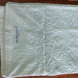 May include: A white cotton fabric with a textured, embossed design. The fabric has a label that reads "Sunshine Textile Store".
