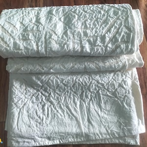 May include: A stack of three white, textured, cotton fabric panels. The fabric has a crinkled, wrinkled, or embossed look.