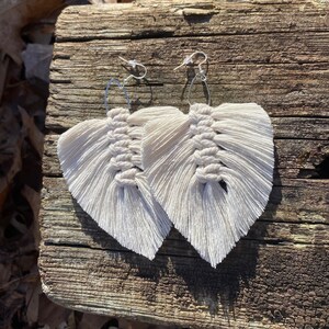 May include: A pair of white feather earrings with silver hooks. The earrings are made of macrame and have a fringe design.