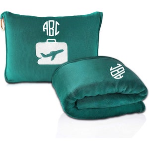 Puede incluir: Una manta de viaje de color turquesa con una almohada a juego. La almohada tiene un dise&ntilde;o blanco de avi&oacute;n y maleta con las letras "ABC" bordadas en un c&iacute;rculo. La manta tambi&eacute;n tiene las letras "ABC" bordadas en un c&iacute;rculo.