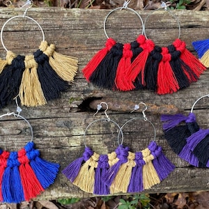 May include: Six pairs of hoop earrings with colorful tassel fringe. The tassels are made of yarn in various colors, including red, blue, black, gold, and purple. The hoops are silver.