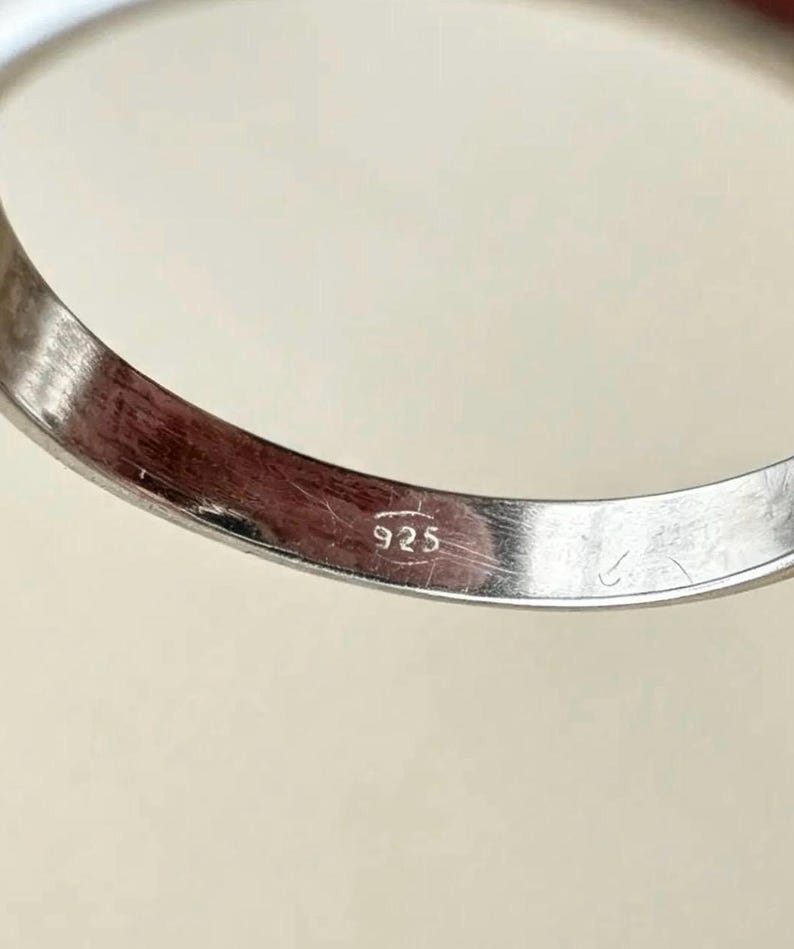 May include: A silver-coloured metal ring band featuring a smooth, polished finish. The interior surface of the band is clearly stamped with the hallmark 925, indicating the metal composition. The ring has a simple, curved, and continuous circular shape.